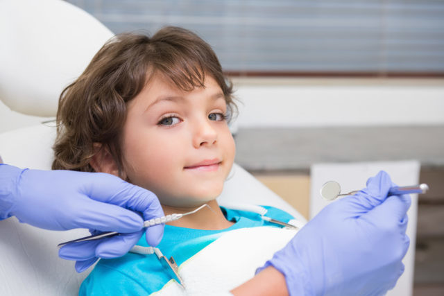 Pediatric dentist examining a little boys teeth in the dentists chair at the dental clinic